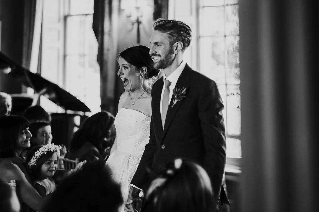 Bride & Groom smiling and cheering at the front of the ceremony room at Hampton Court House Wedding.