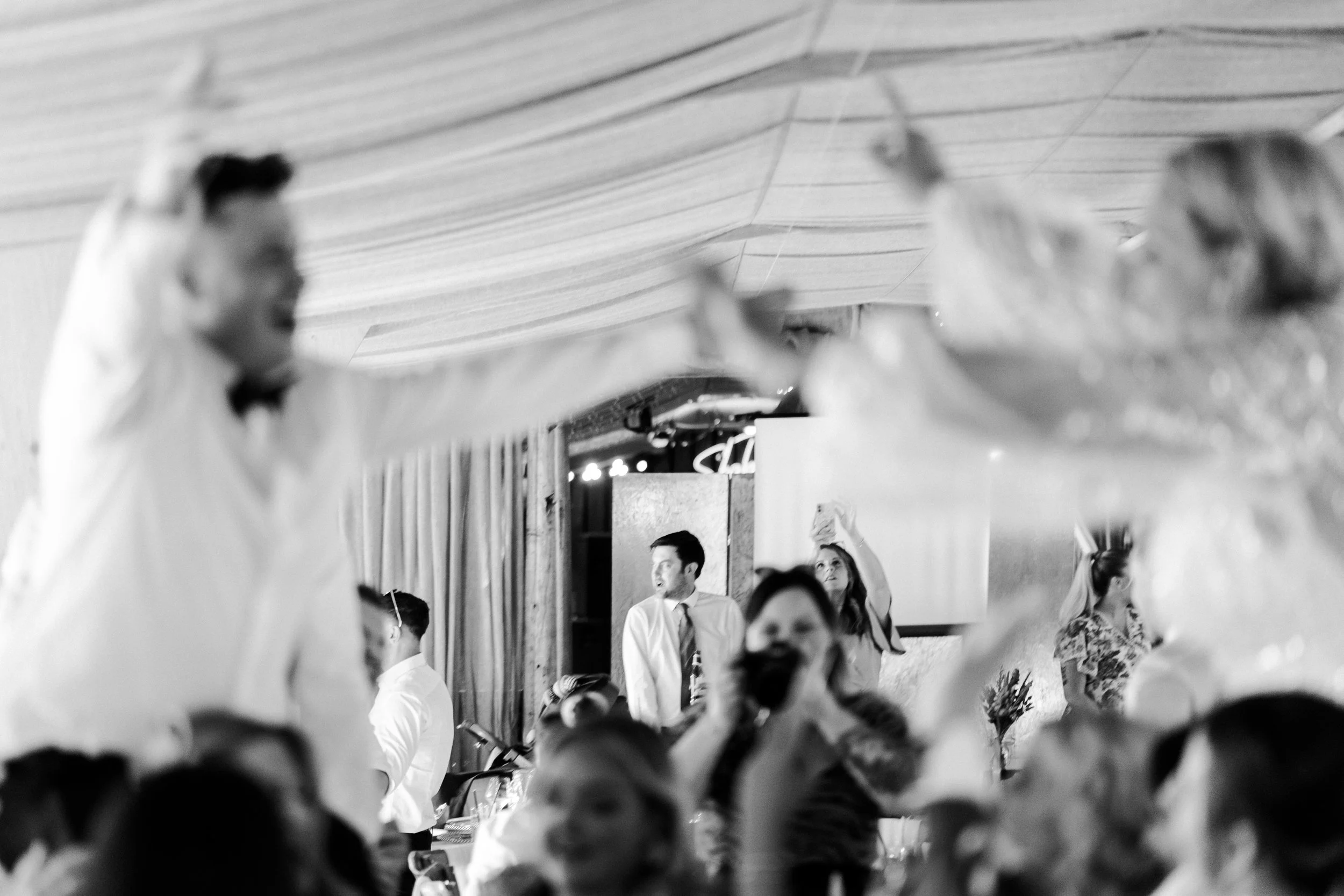 Wedding couple on guests' shoulders blurred with guests in focus in background at a rhyse farm wedding