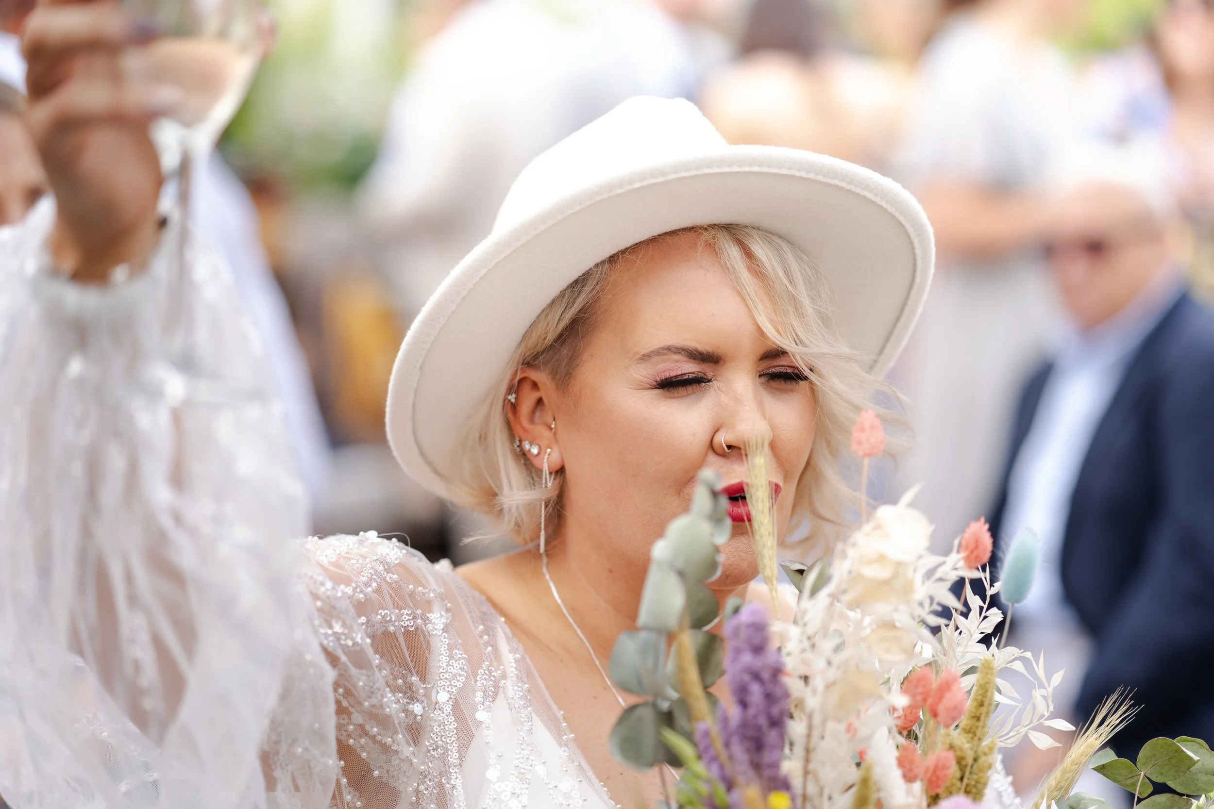 bride holding her bouquet up towards her face and eyes squinting while also toasting with a glass of champagne at a rhyse farm wedding