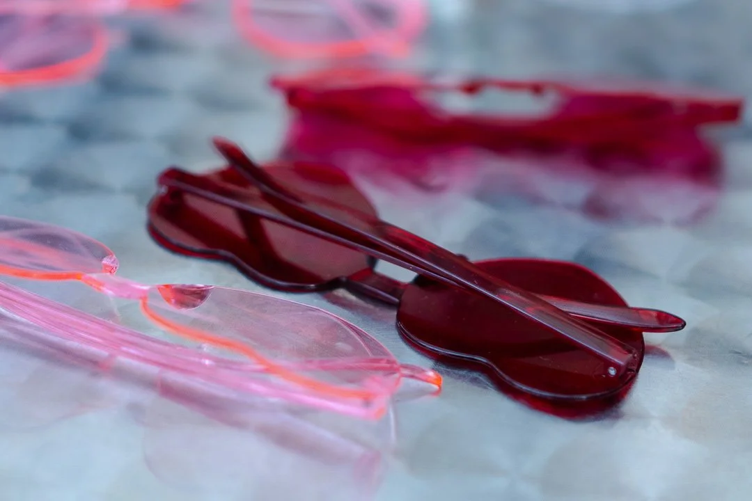 A row of heart-shaped sumglasses in both red and pink on a table at a Hampton Court House Wedding.