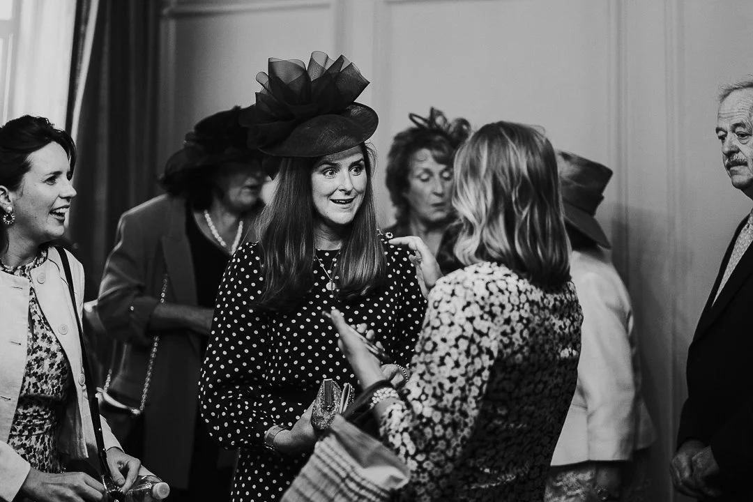 Groom's Sister with a slight smile on her face speaking to a guest in the ceremony room at the Old Marylebone Town Hall Wedding