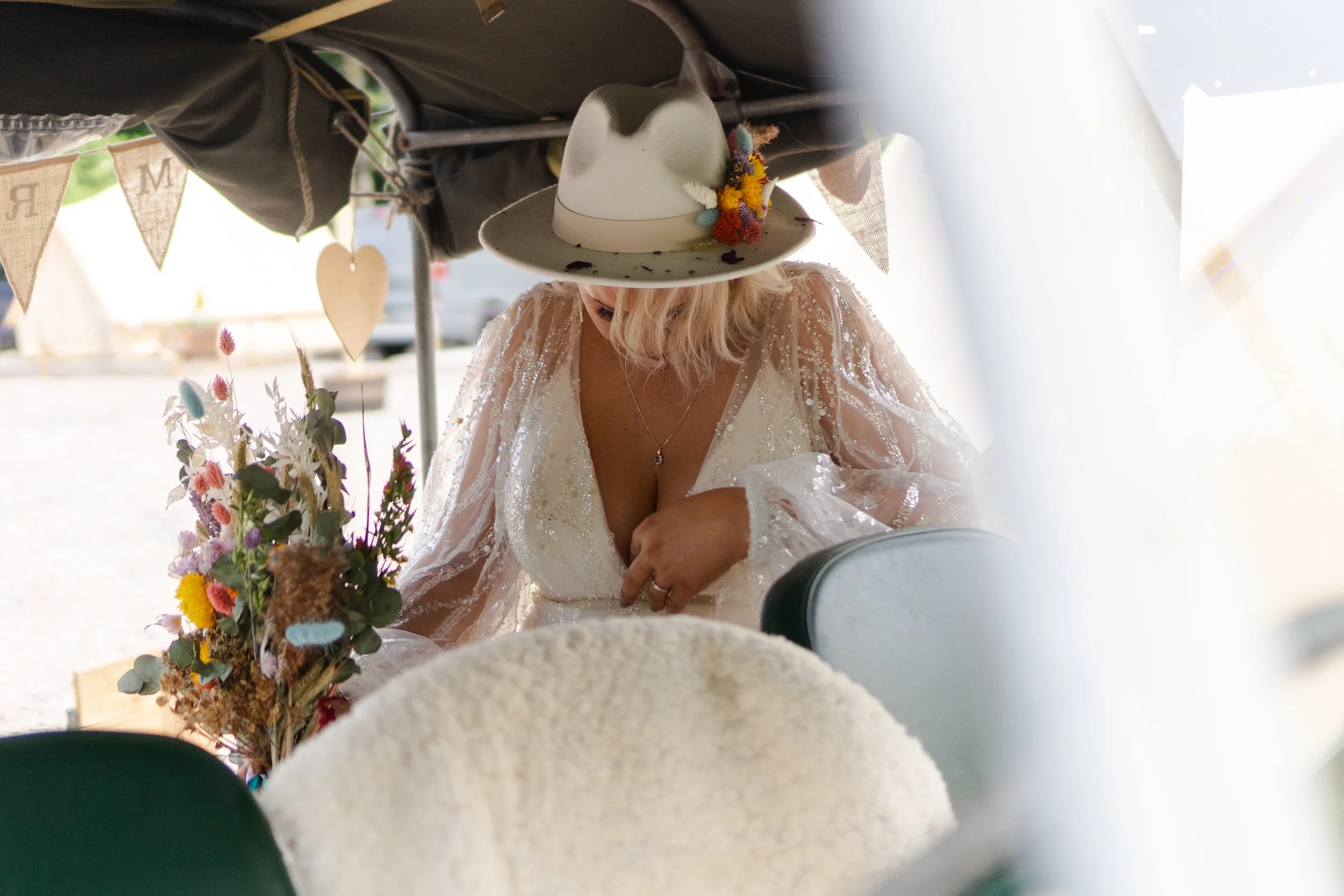 Bride on the back of open top Land Rover fixing her dress at a rhyse farm wedding