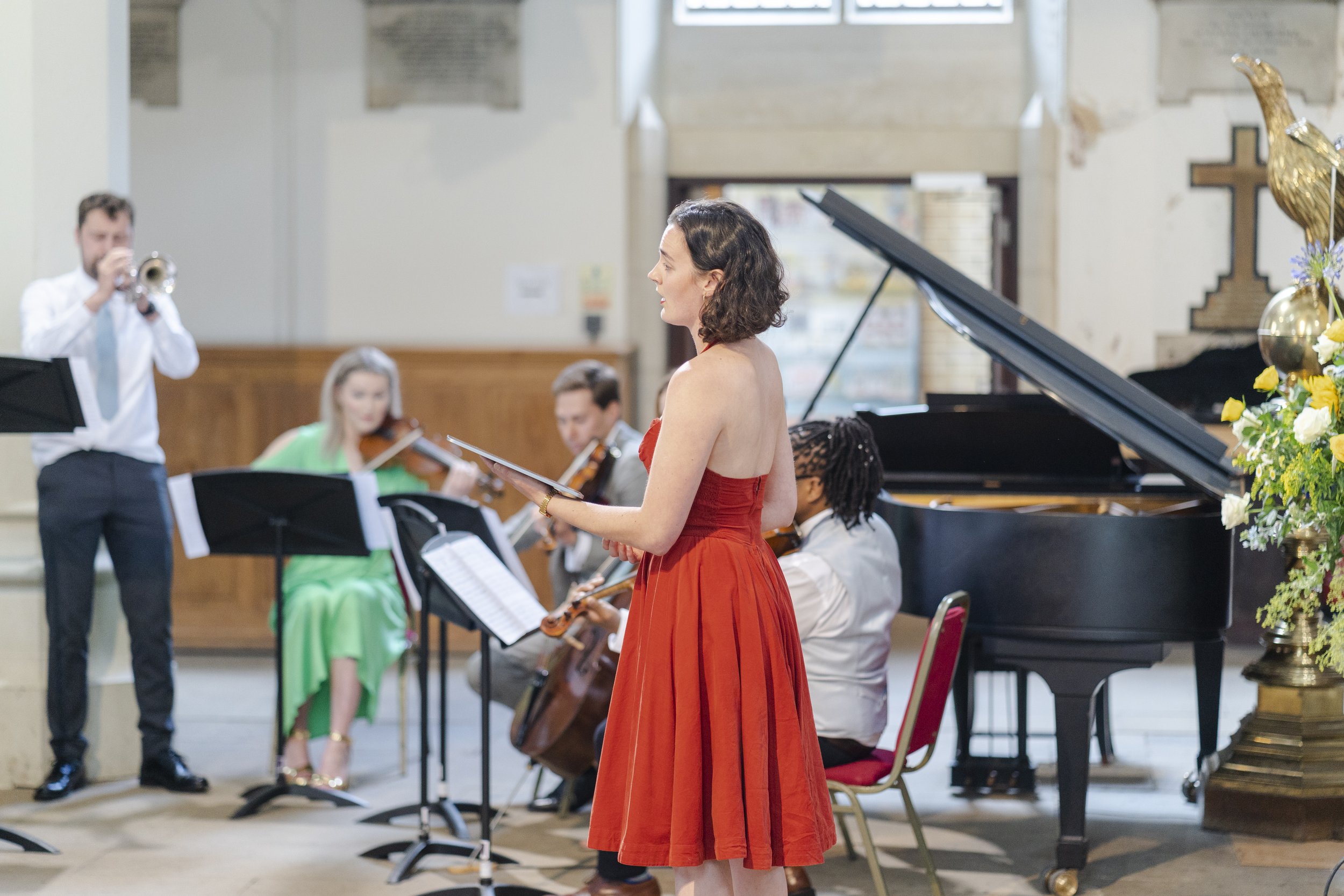 Singer in a red dress at the front of the St Michael's Church with a small orchestra at a Highgate, London Wedding
