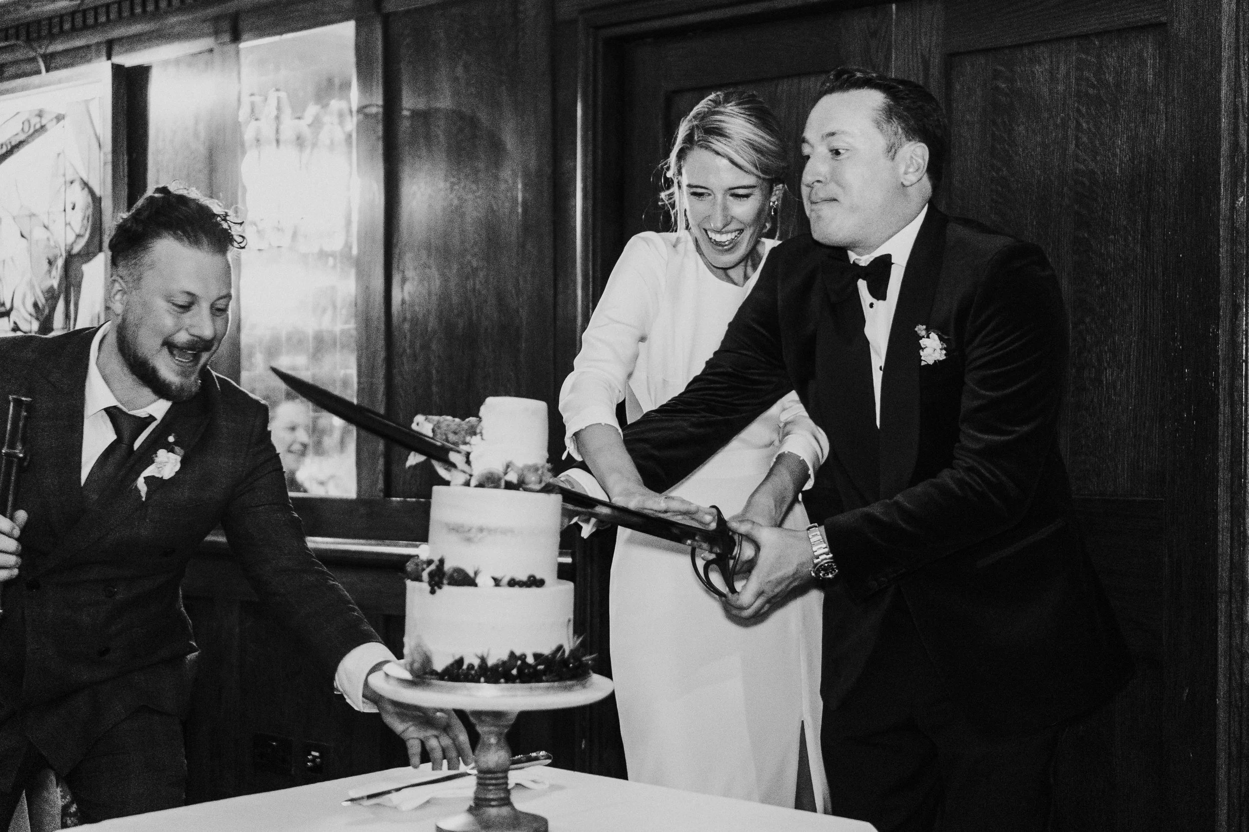 Wedding couple cutting the cake with a sword at The Ivy Restaurant at a Old Marylebone Town Hall Wedding.