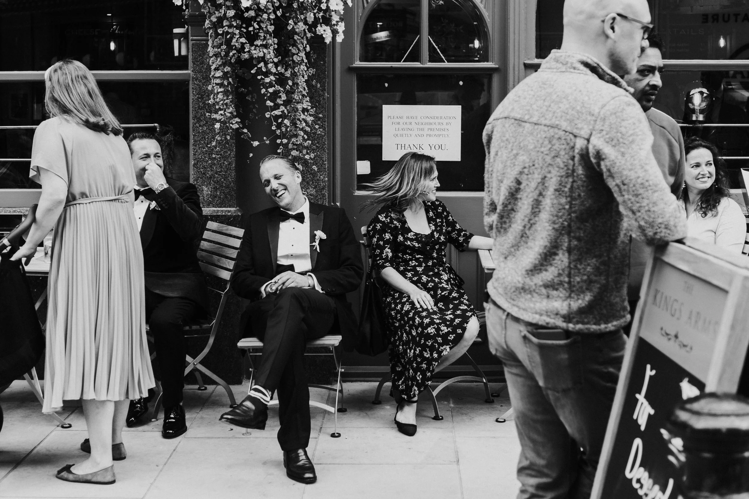 Wedding guests sitting outside a pub laughing with the Groom at a Old Marylebone Town Hall Wedding.