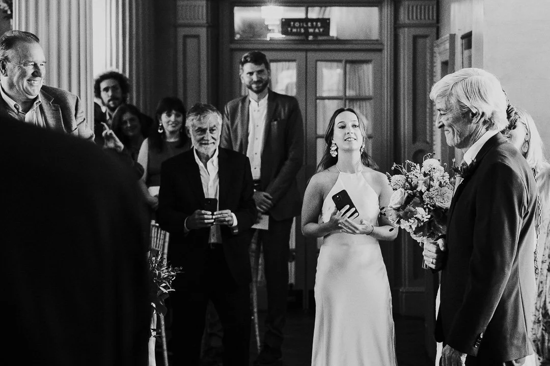 Bride and her father walking into the ceremony with guests either side of the small aisle.