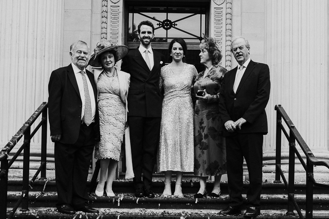 Wedding couple with both sets of parents posing for a group shot on the top step outside at the Old Marylebone Town Hall Wedding.