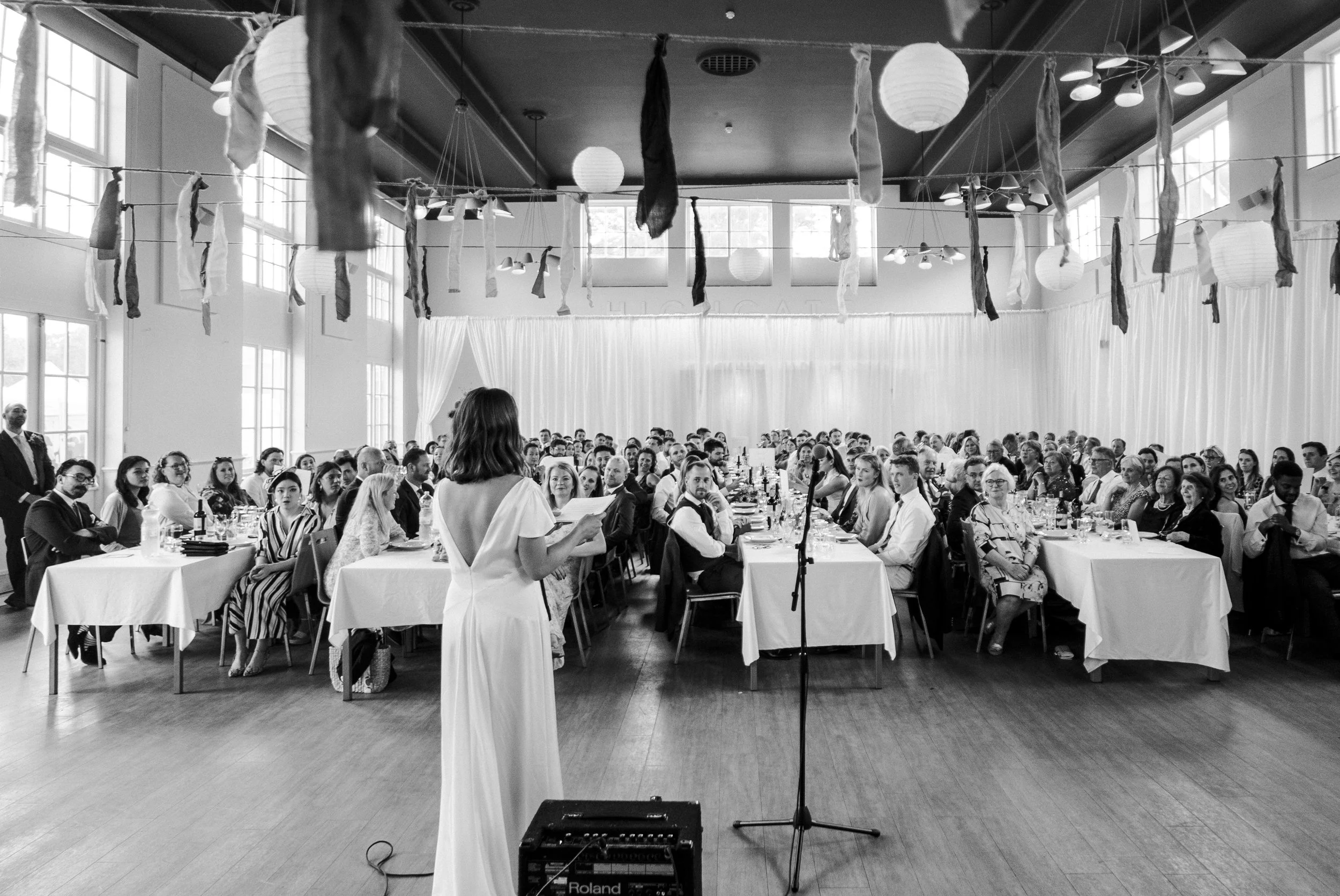 Bride facing the reception wedding tables giving a speech at Highgate School at a Highgate, London Wedding.