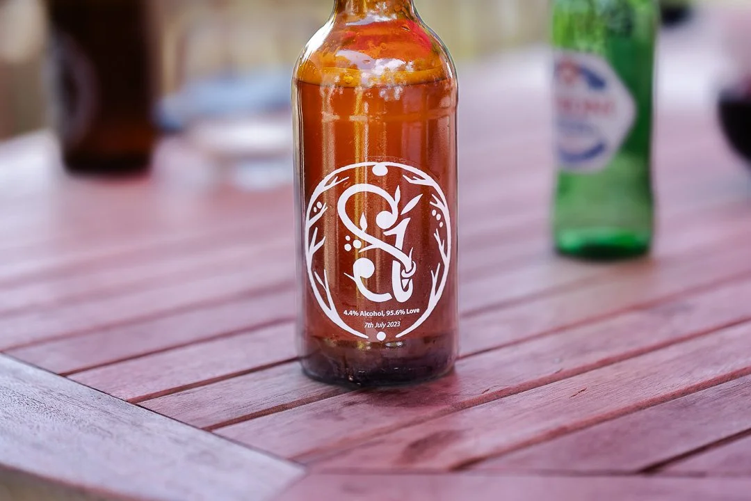 A single Beer Bottle with the couples' logo initials on sitting on a table at a Hampton Court House Wedding.