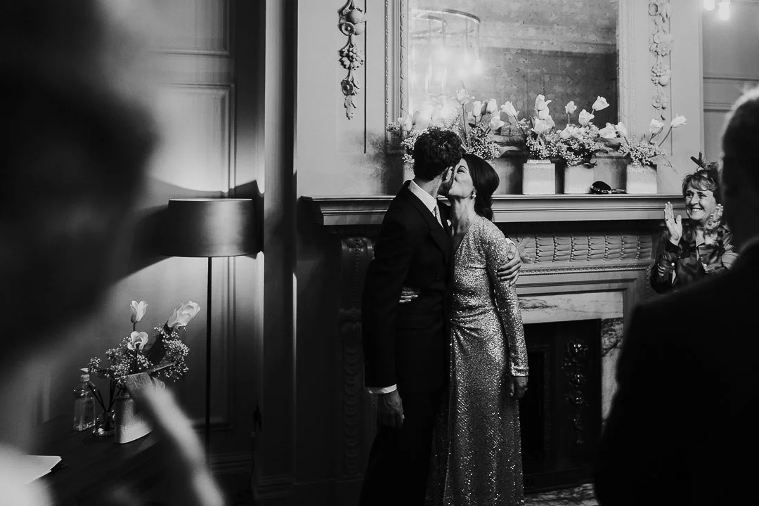 Wedding couple kissing with guest clapping and congratulating them in the ceremony room at the Old Marylebone Town Hall Wedding.