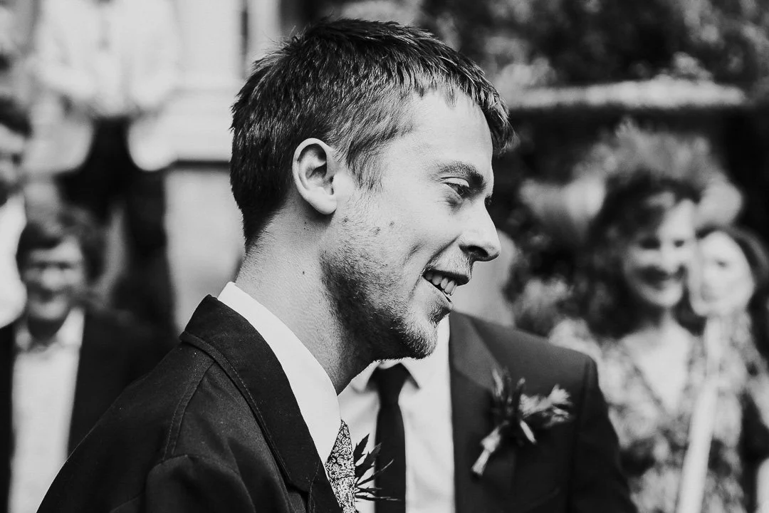 A guest smiling while listening to a another guest out of shot talking at a Hampton Court House Wedding.