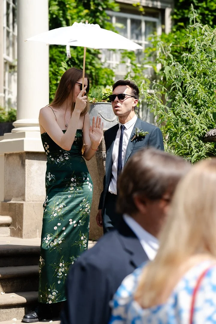 Two guests standing on the front porch steps under a white parasol at a Hampton Court House Wedding.