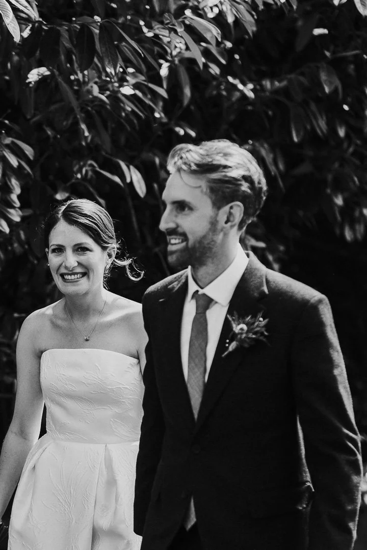 Bride smiling at the camera while walking through the gardens with the groom at Hampton Court House at London Wedding.