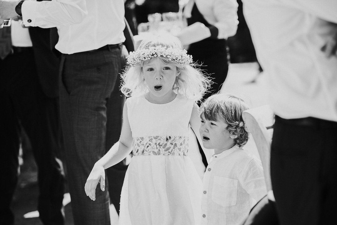 Flowergirl wearing a flower crown standing and looking at the camera with a toddler who is looking away from the camera at a Hampton Court House Wedding,