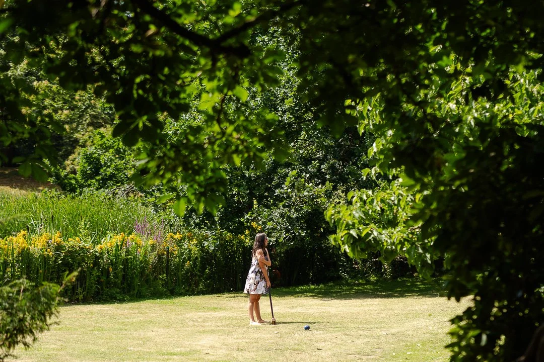 One guest with a croquet mallet and a ball on the Hampton Court House lawn at a London Wedding.