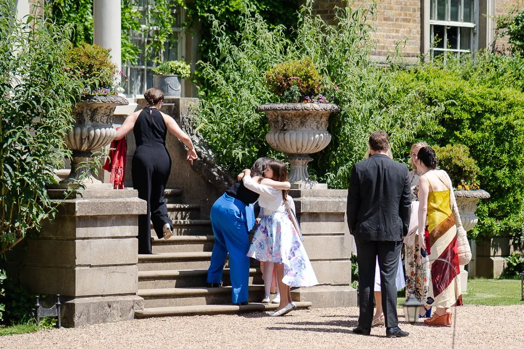 Guests on the front steps walking up twoards the door with some hugging each other before a Hampton Court House Wedding