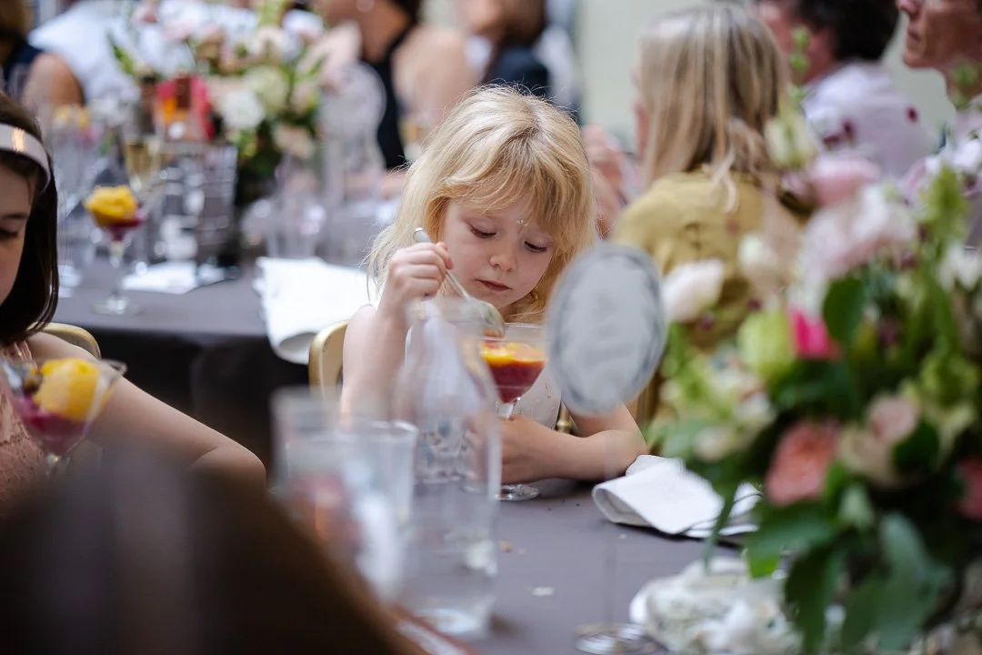 A young guest with a spoon eating a dessert out of a cocktail glass at the dinner table at a Hampton Court House Wedding.