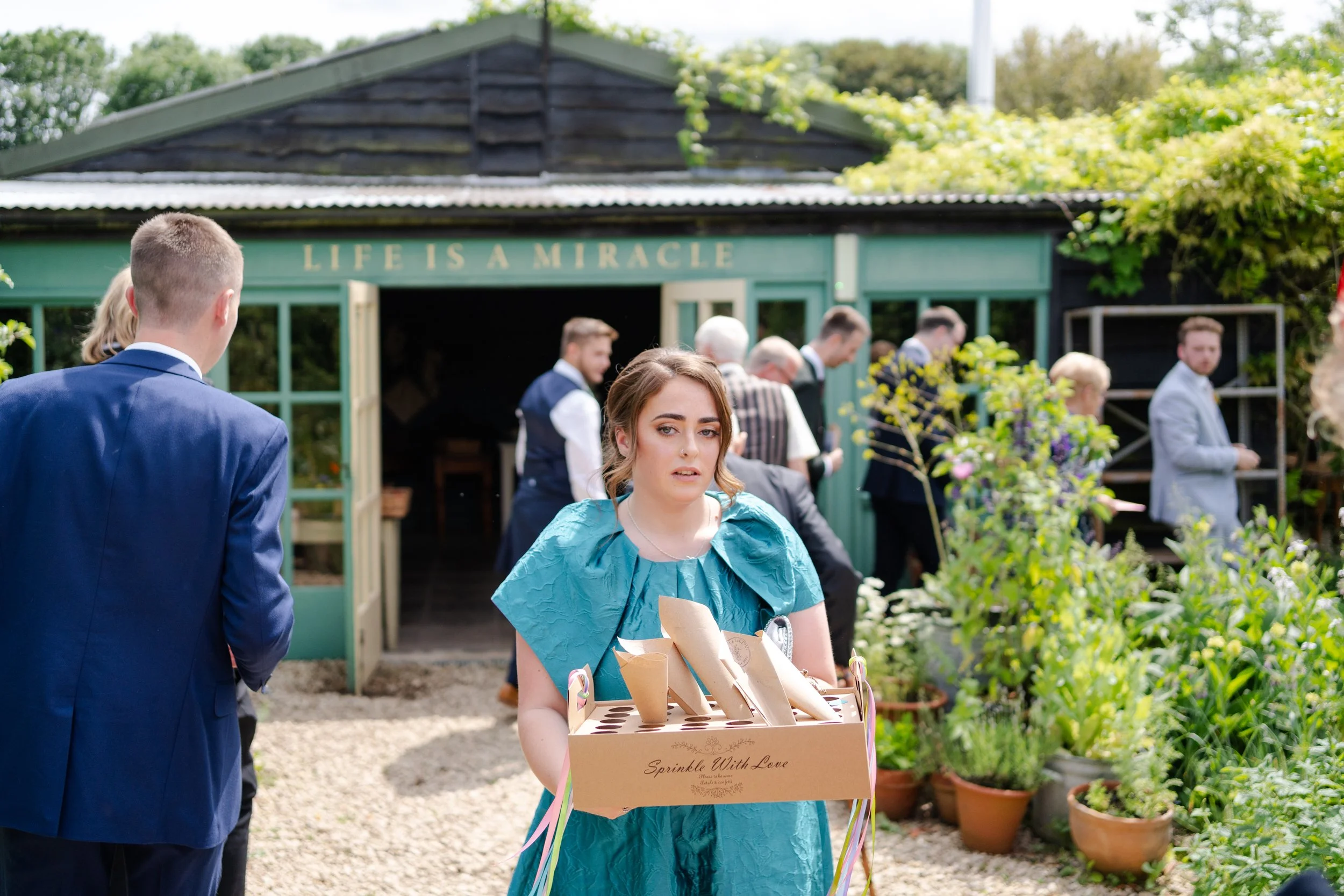 Bridesmaid collecting confetti cones from guests at a Worton Kitchen Garden, Oxfordshire Wedding.