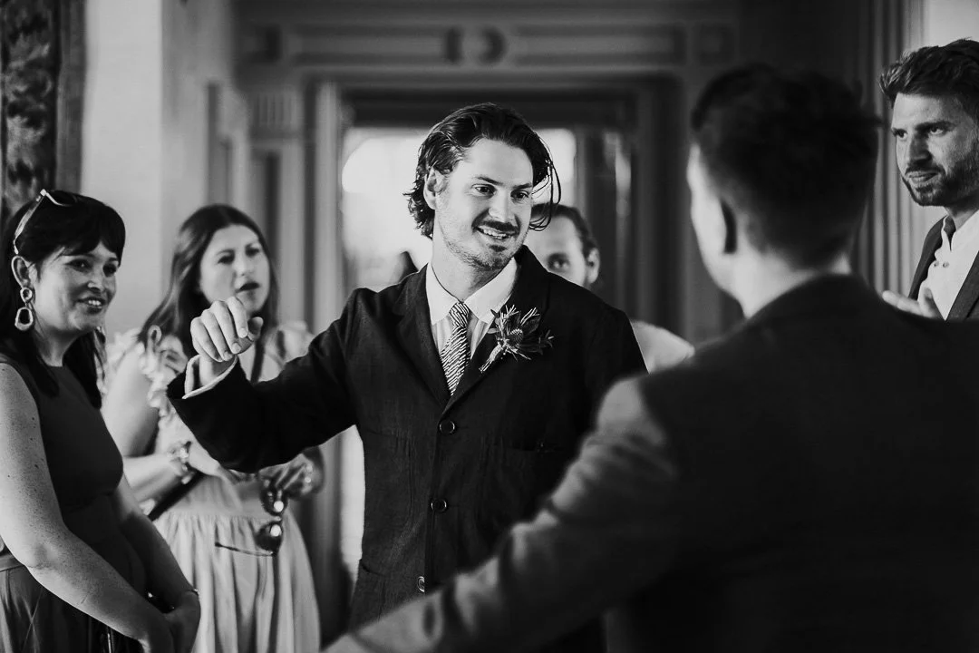 Groomsman in the middle of the image preparing to greet another guest in the ceremony room at a Hampton Court House Wedding