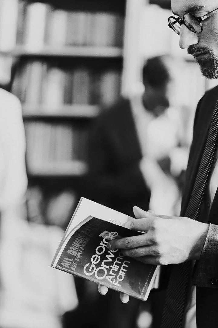 Groomsman in Hampton Court House's Library standing and reading Animal Farm book