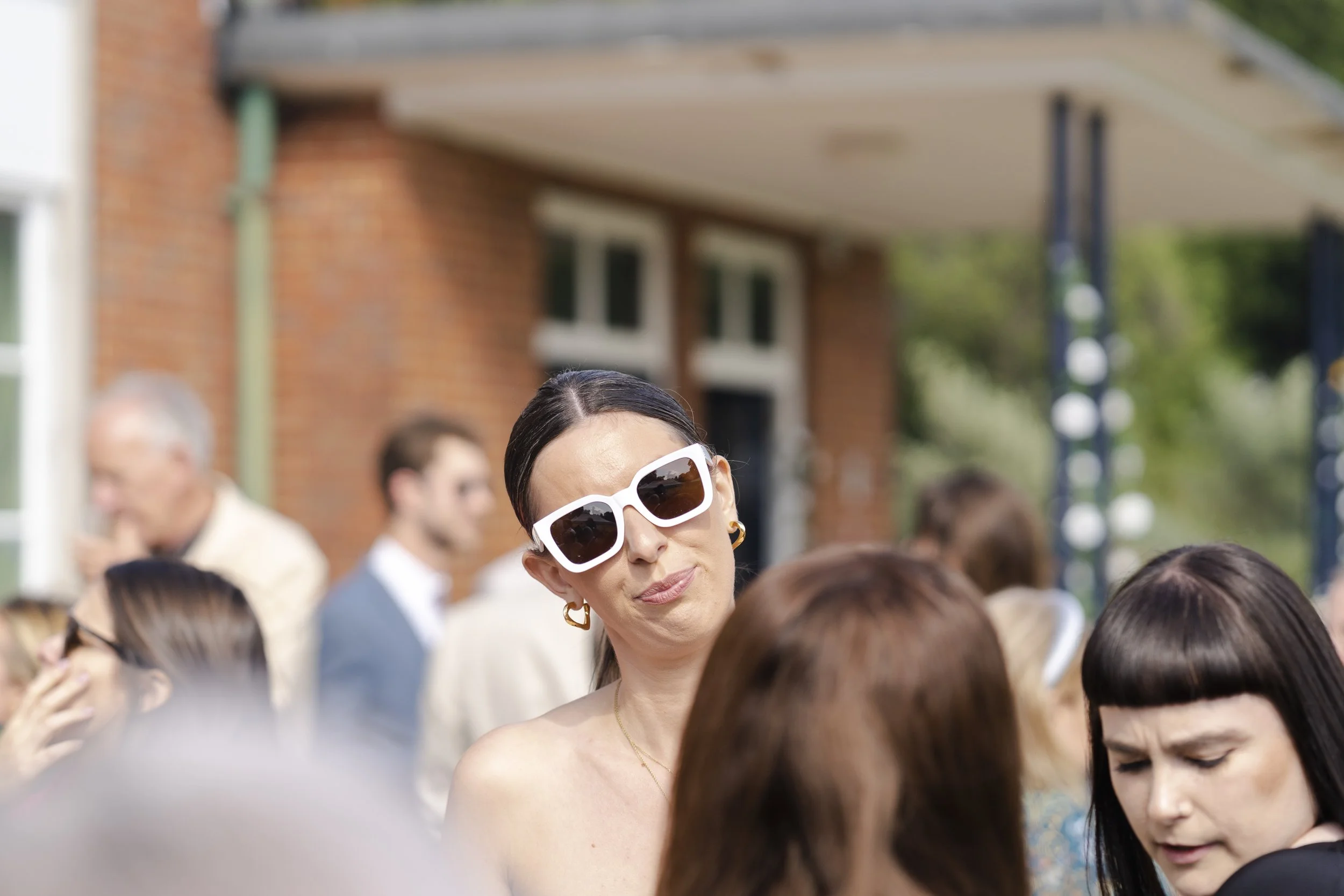 Wedding guest wearing sunglasses and looking with a slight smile at the camera at a Highgate, London Wedding.