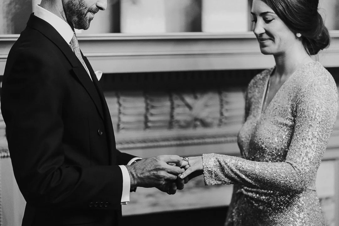 Couple holding hands while the Groom slips the wedding ring onto the Bride's finger in the ceremony room at the Old Marylebone Town Hall Wedding.