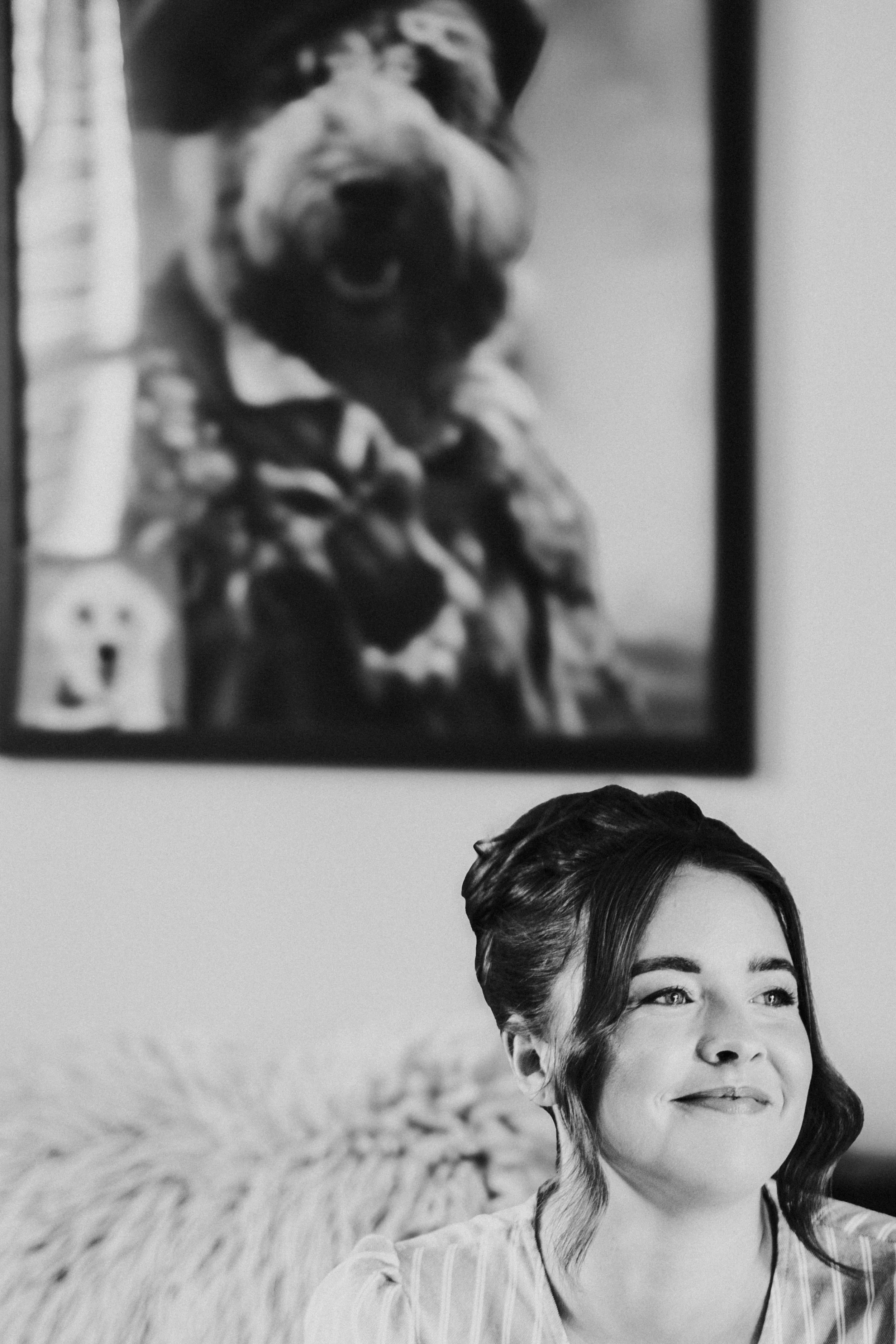 Bride sitting on the sofa smiling under a portrait of a dog for a Worton Kitchen Garden Wedding Photography