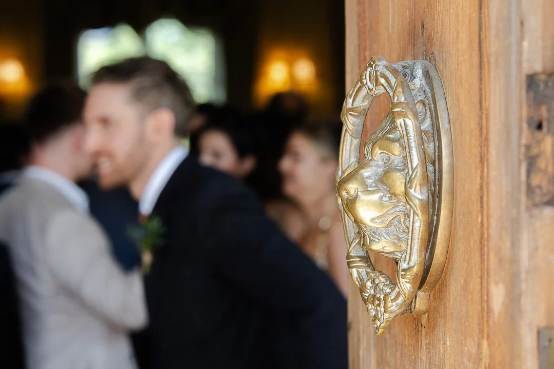 A lion door knocker on the front door of Hampton Court House with the groom in the background blurred at a London Wedding.