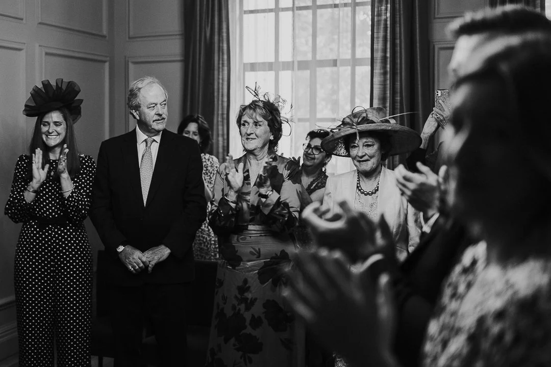 Groom's Mum, Sister and Bride's mum clapping while Groom's dad looks around proudly in the ceremony room at the Old Marylebone Town Hall Wedding.
