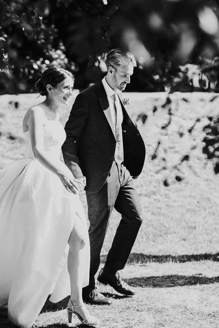 Wedding couple walking hand in hand in the gardens at Hampton Court House with the bride smiling at a Surrey Wedding.