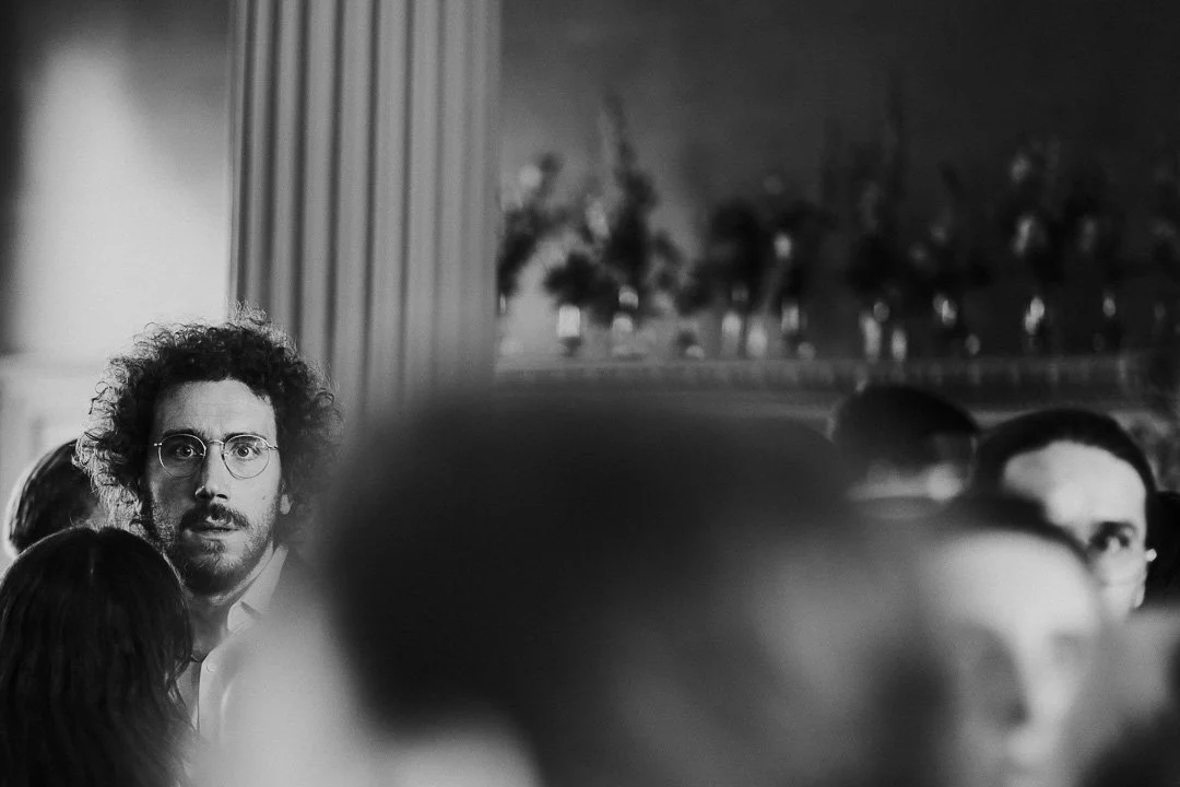 A Guest at a Hampton Court House wearing glasses staring forward with a small crowd in foreground allowing only his head to be in focus.