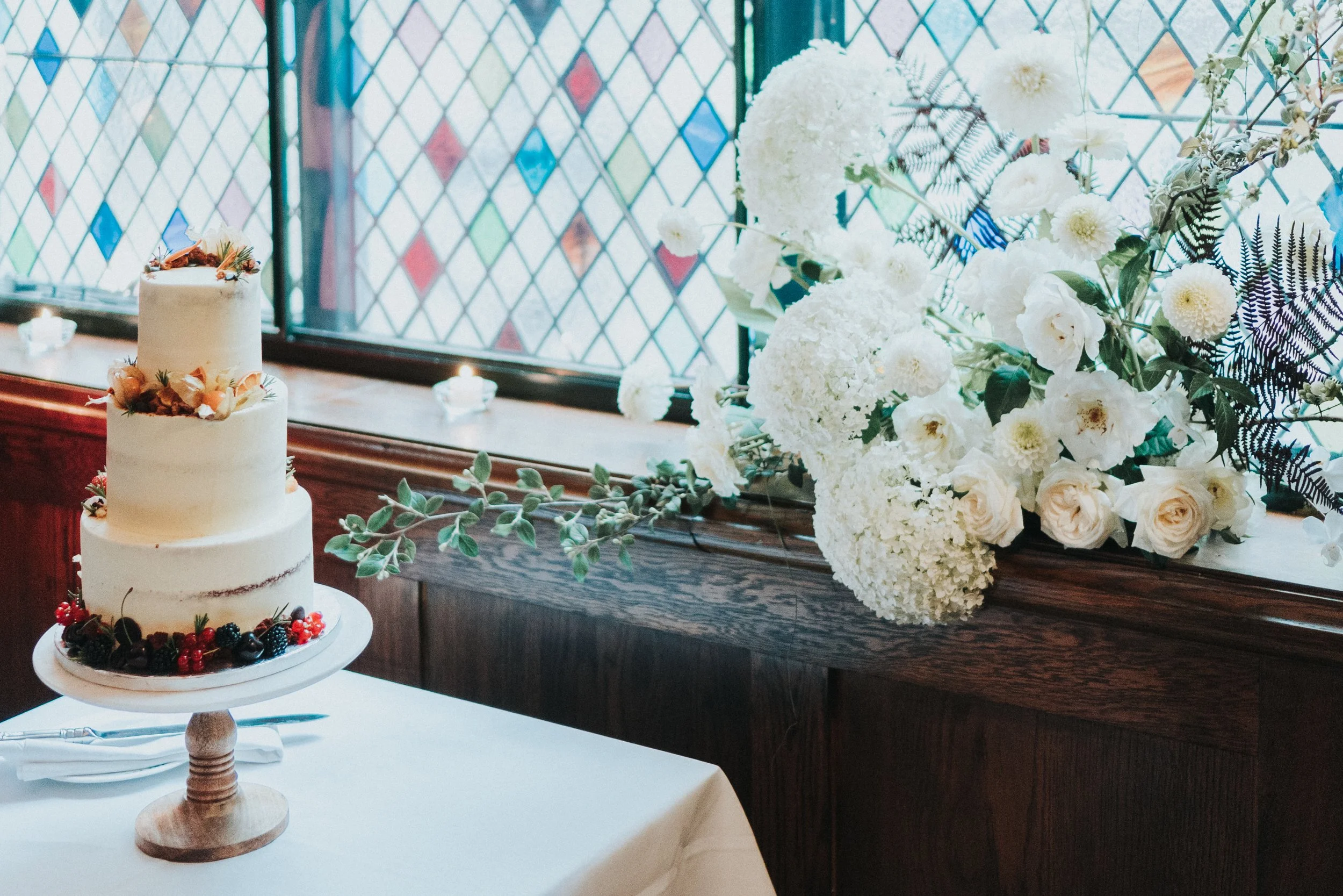 Wedding cake on a table next to stained glass windows in The Ivy Restaurant at a Old Marylebone Town Hall Wedding.