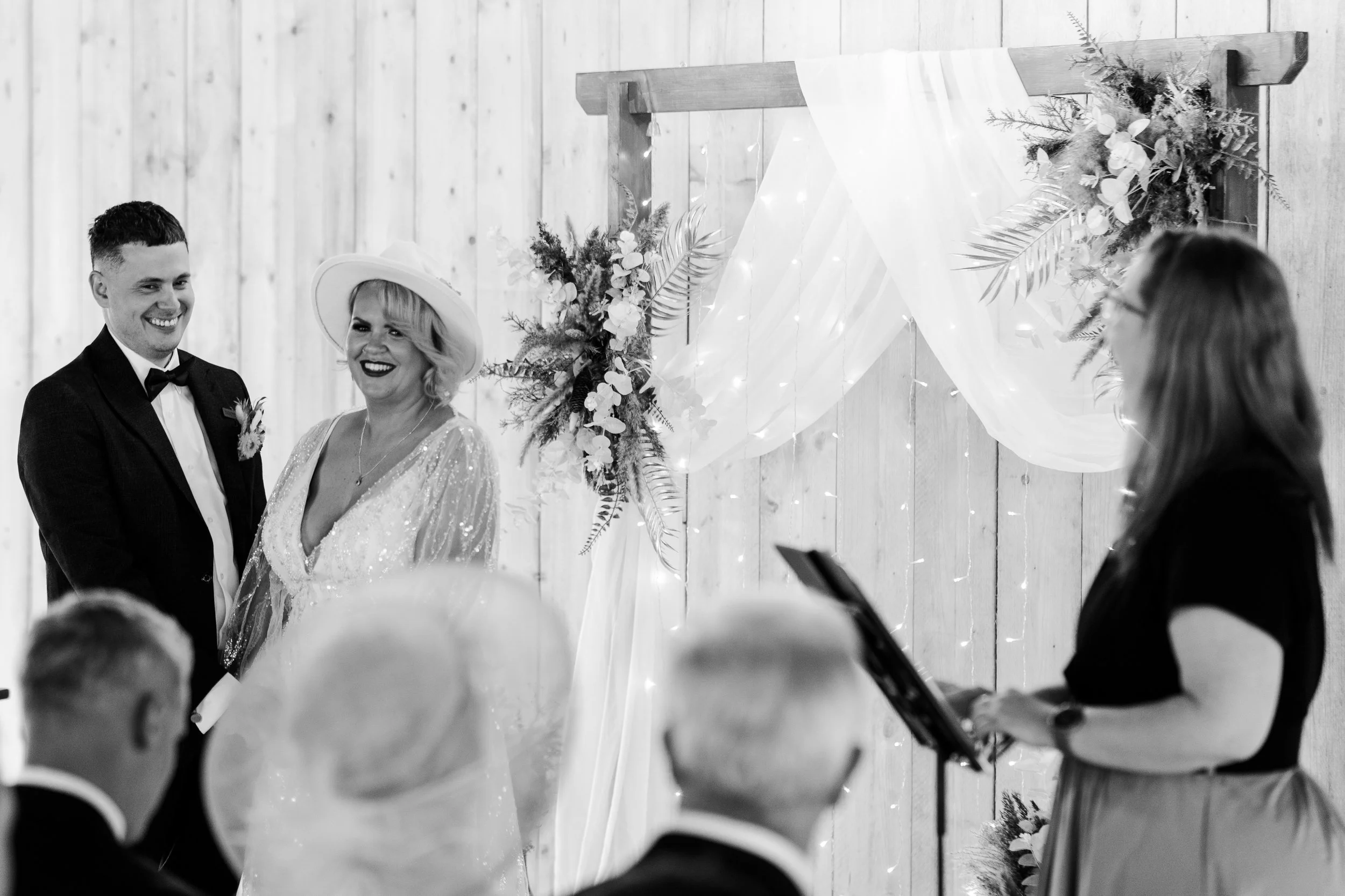 Wedding couple at the front of the ceremony barn holding hands and smiling towards the guest and celebrant at a rhyse farm wedding