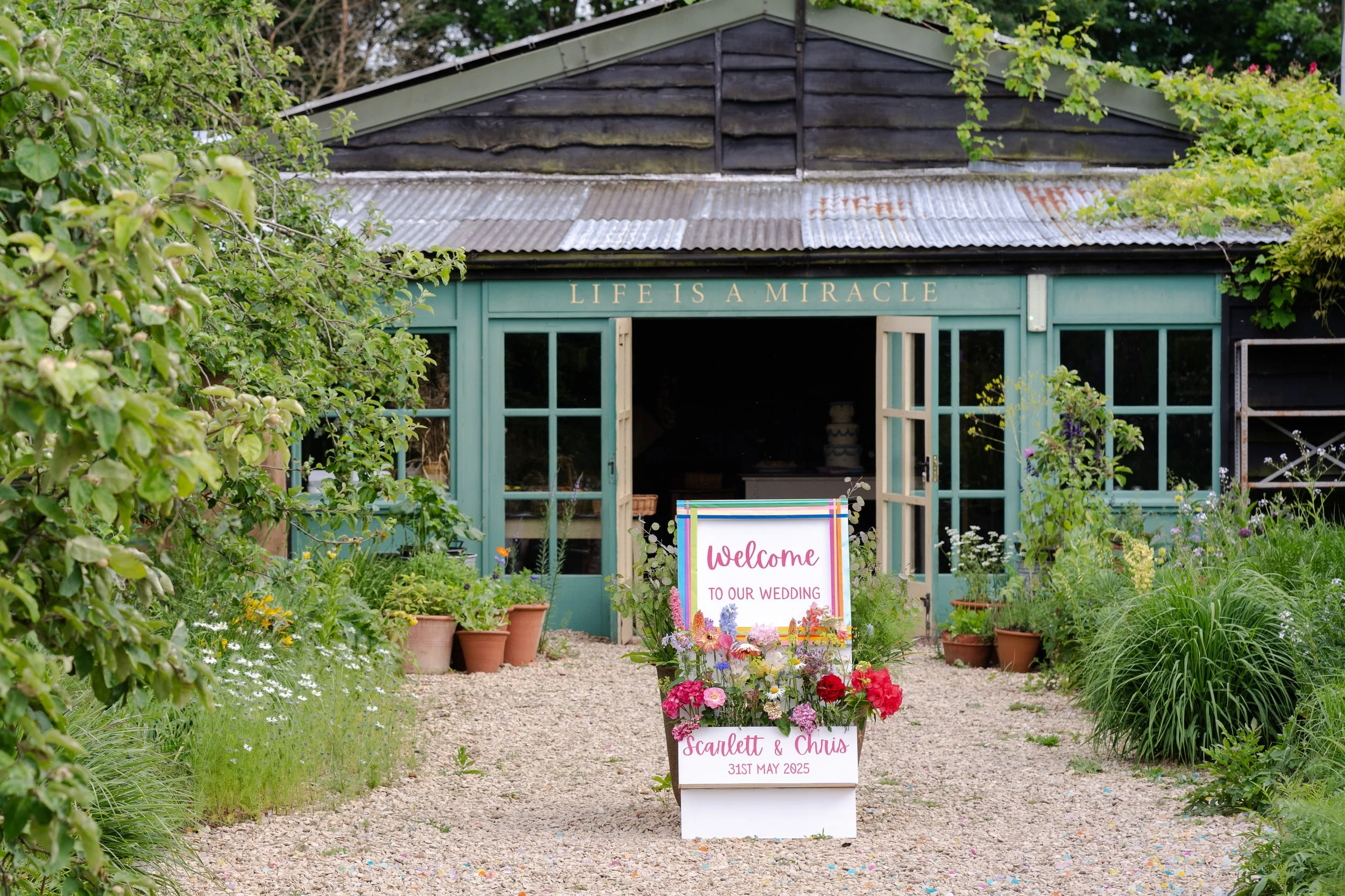 Welcome sign with a flower arrangement for a wedding at Worton Kitchen Garden, Oxfordshire
