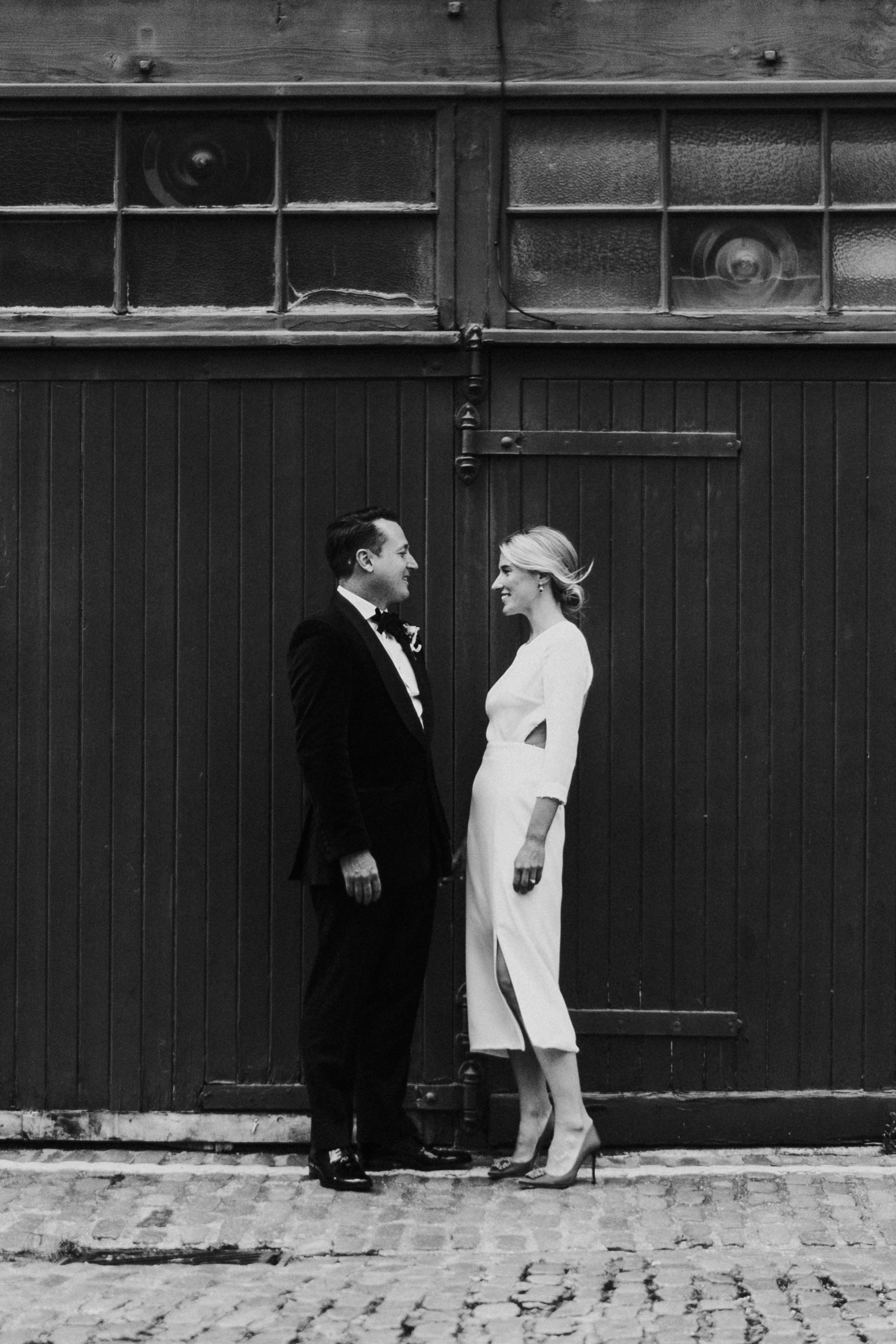 Bride & Groom standing outside wooden doors down a Mews, posing facing each other smiling before a Old Marylebone Town Hall Wedding