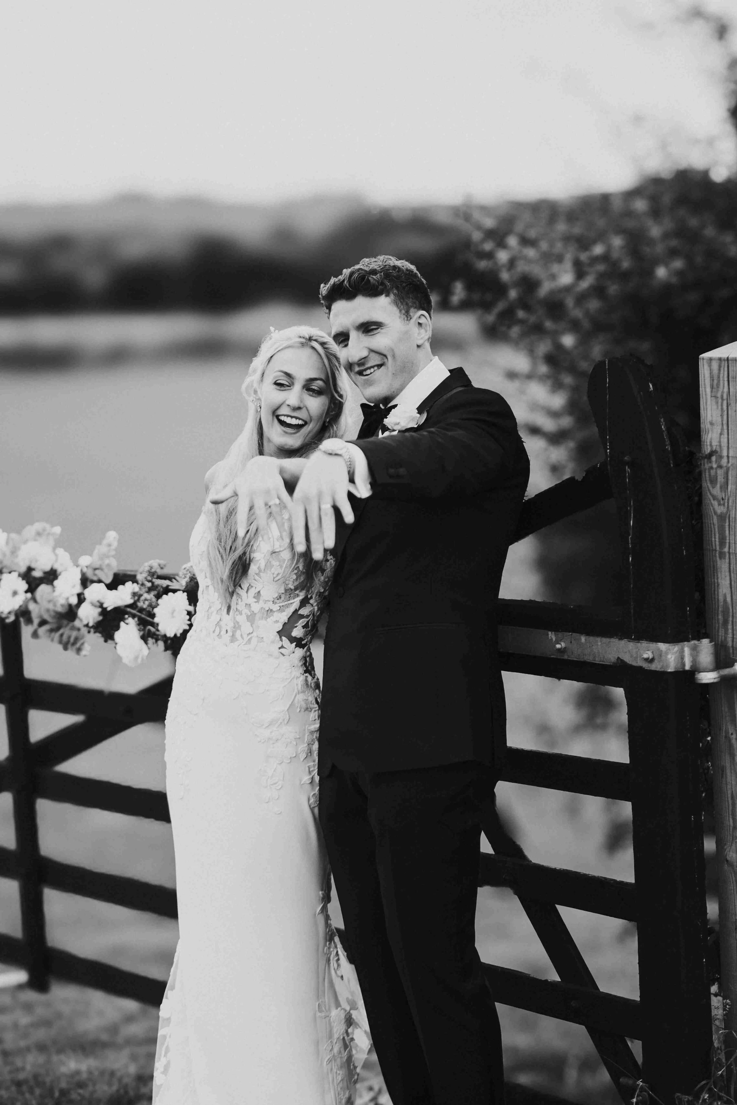 Couple leaning against a wooden gate, showing off their wedding rings at the Halfmoon Farm Wedding in Rutland