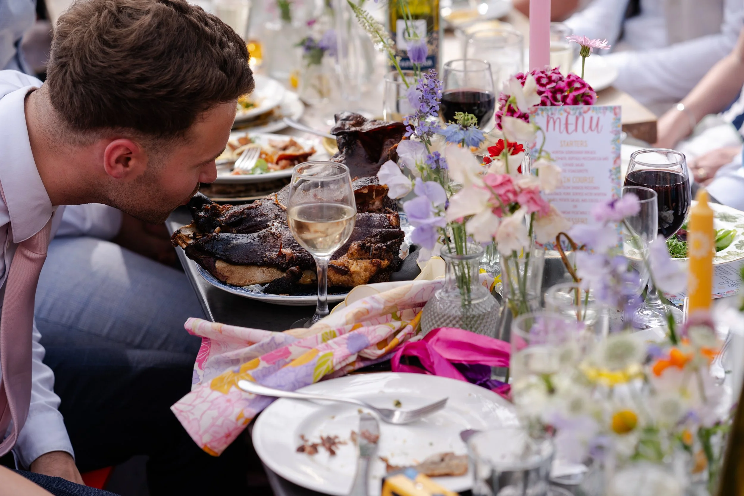 Wedding guest pretending to kiss a cooked pigs head on wedding reception table at a Worton Kitchen Garden, Oxfordshire Wedding.