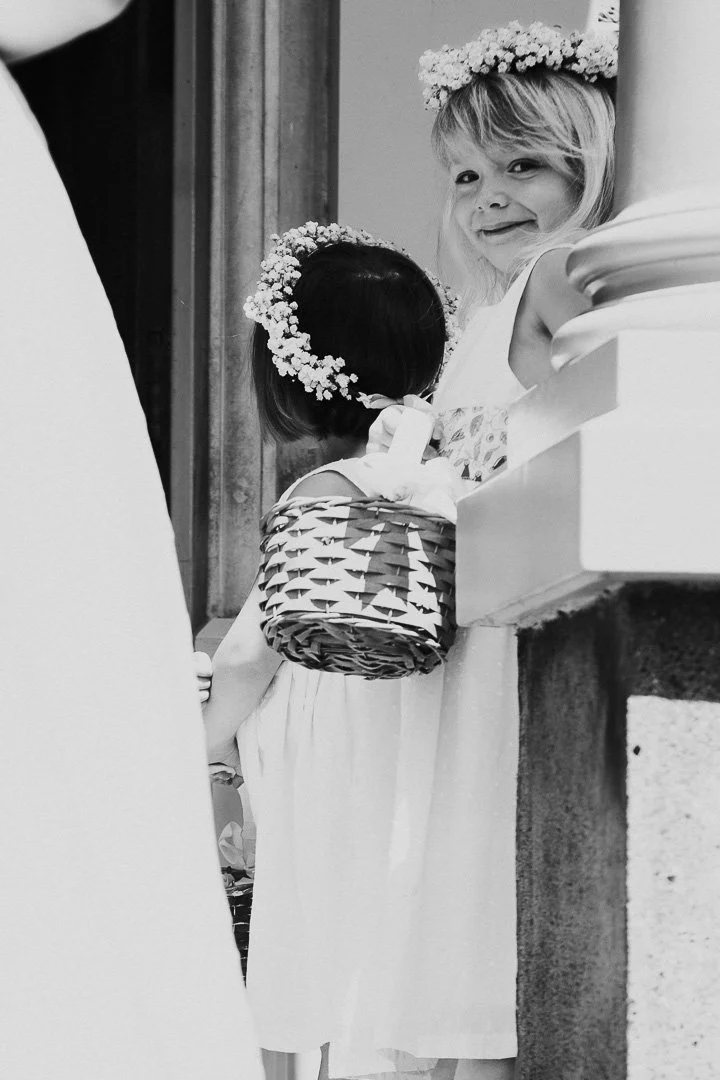 Flowergirls standing outside Hampton Court House before entering the ceremony, one flowergirl turned around and smiling at the camera at Surrey Wedding