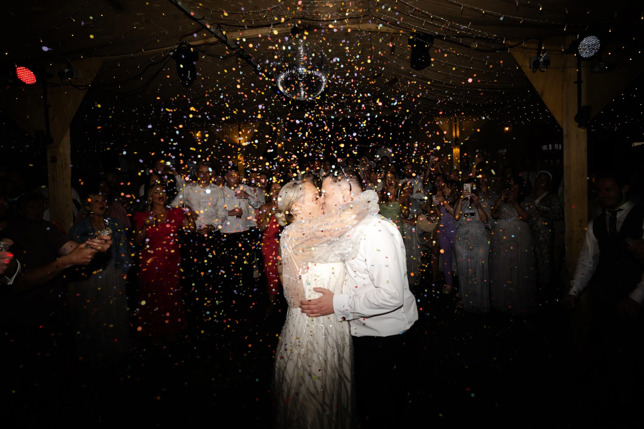 Bride & Groom on the dancefloor holding each other and kissing while a shower of confetti comes down at a rhyse farm wedding