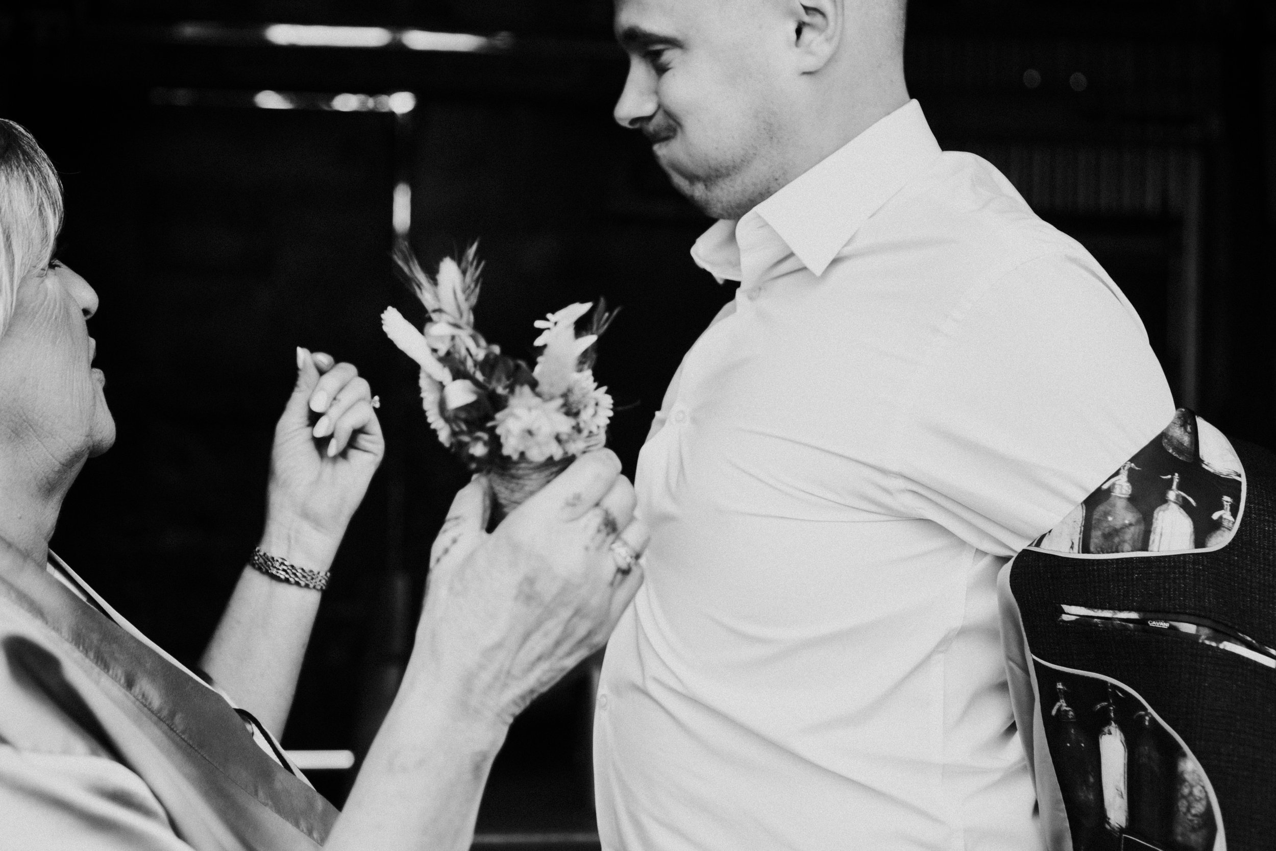 Groom getting his buttonhole put on while puffing his cheeks.