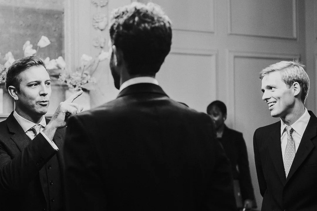 Guests talking to Groom who back is to the camera and another guest smiling in the ceremony room at the Old Marylebone Town Hall Wedding.