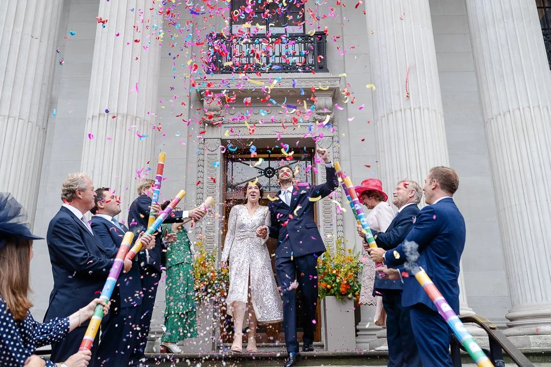 Wedding couple walking down the steps looking up as confetti showers down on them at the Old Marylebone Town Hall Wedding.