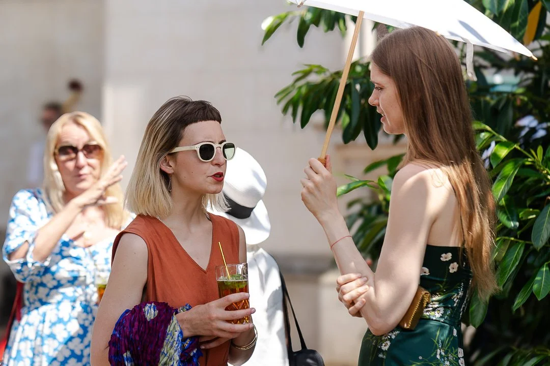 A guest under a parasol talks to another guest wearing sunglasses and holding a glass of Pimms at Hampton Court House Wedding.