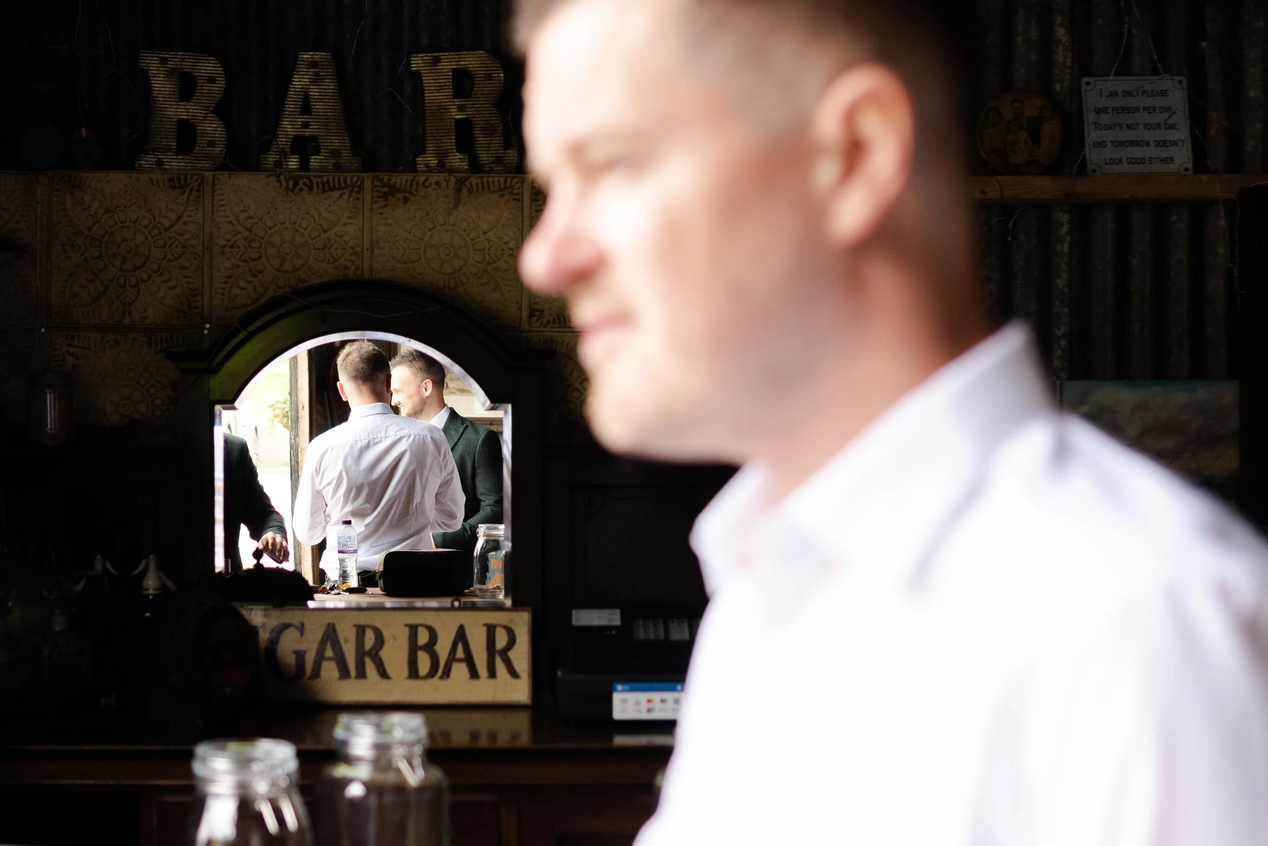 groomsmen standing in front of a mirror which reflecting the groom talking to another groomsmen at a rhyse farm wedding