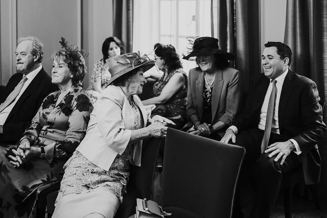 Bride's Mum leaning behind to speak and laugh with guests in the ceremony room at the Old Marylebone Town Hall Wedding.
