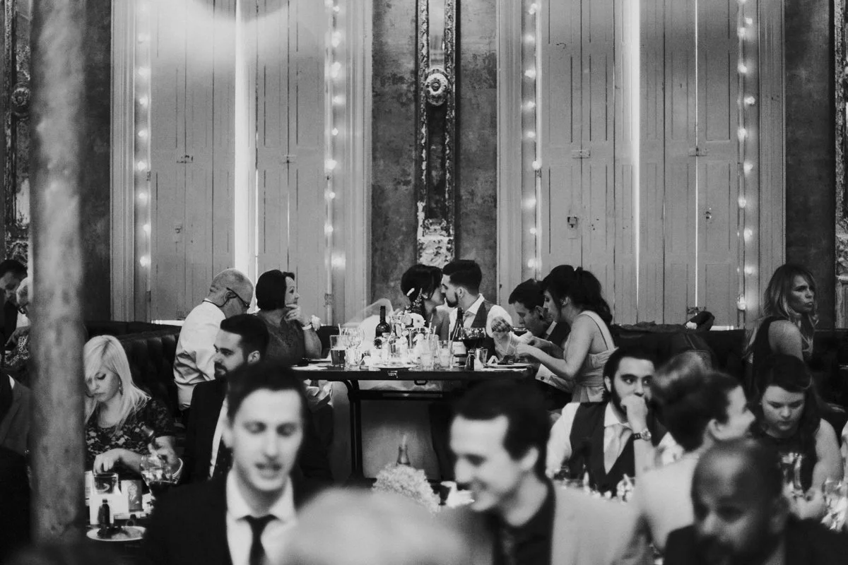 A image shot through the guest of the Bride & Groom kissing at the top table of their wedding reception at the iconic The Old Queens Head, Essex Road, Islington at a London Wedding