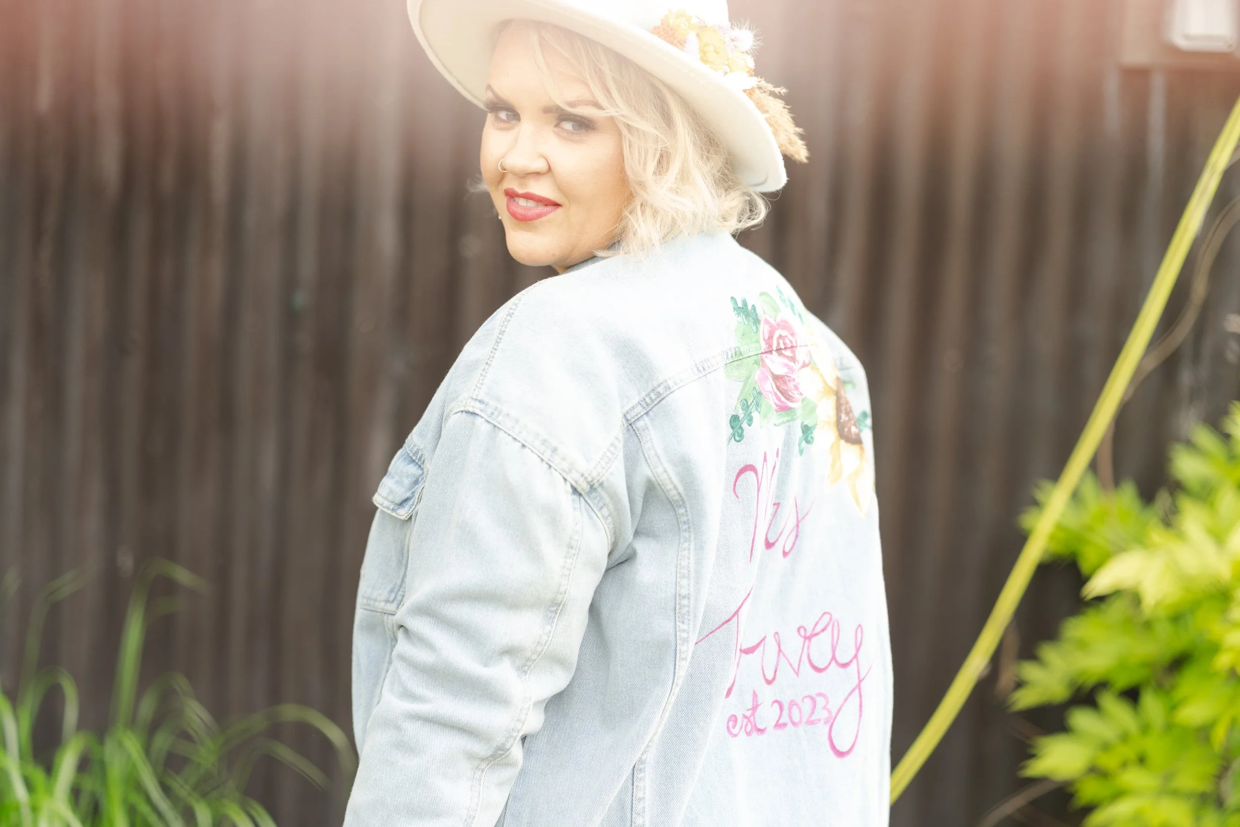 Bride looking over her shoulder smiling wearing a denim jacket with writing on the back at a rhyse farm wedding