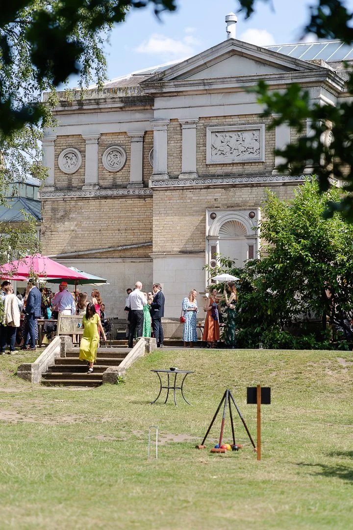 A side view of the venue from the lawn with guest mingling around at a Hampton Court House Wedding.