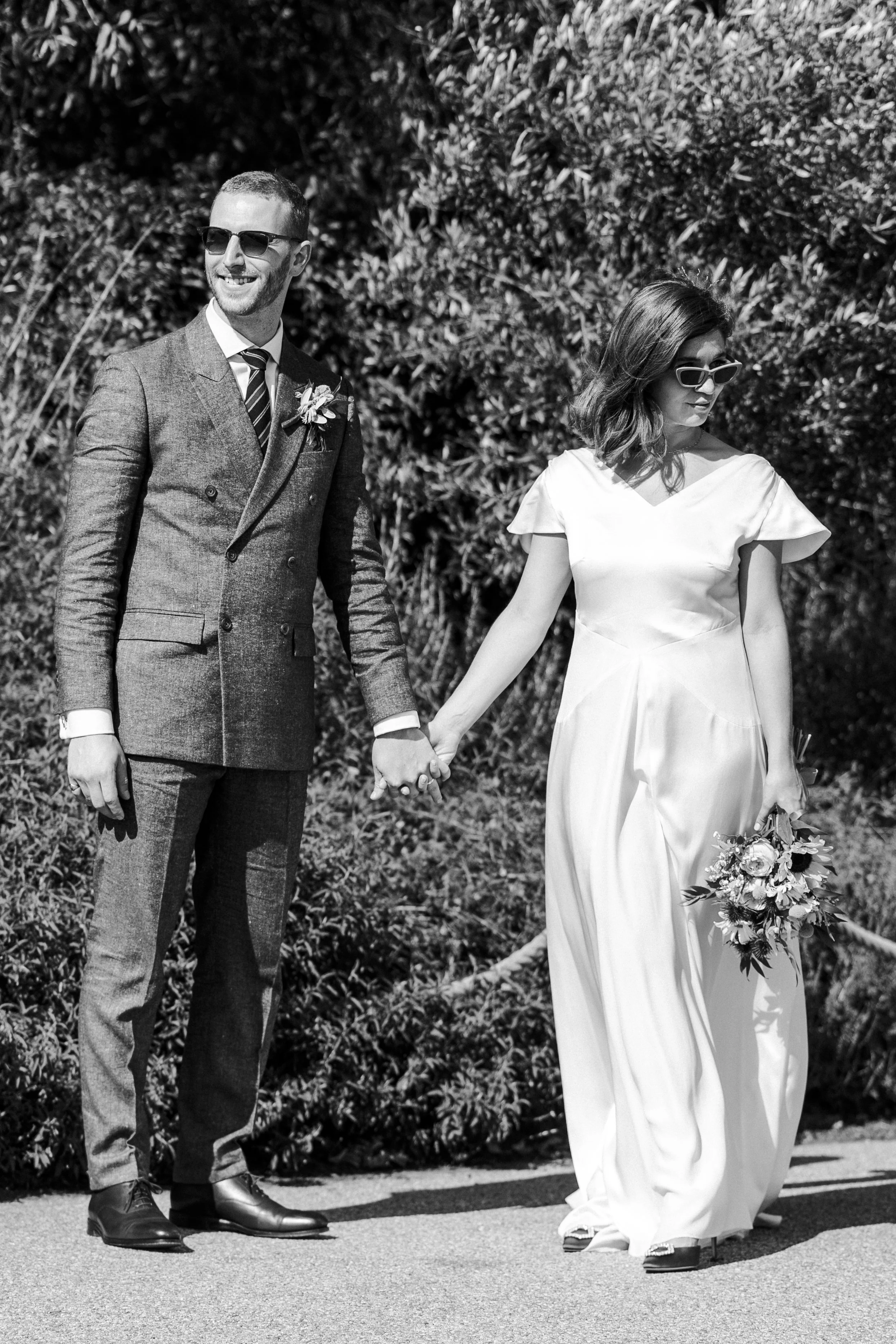 Wedding couple posing for portraits wearing sunglasses standing holding hands but looking opposite ways at a Highgate, London Wedding.