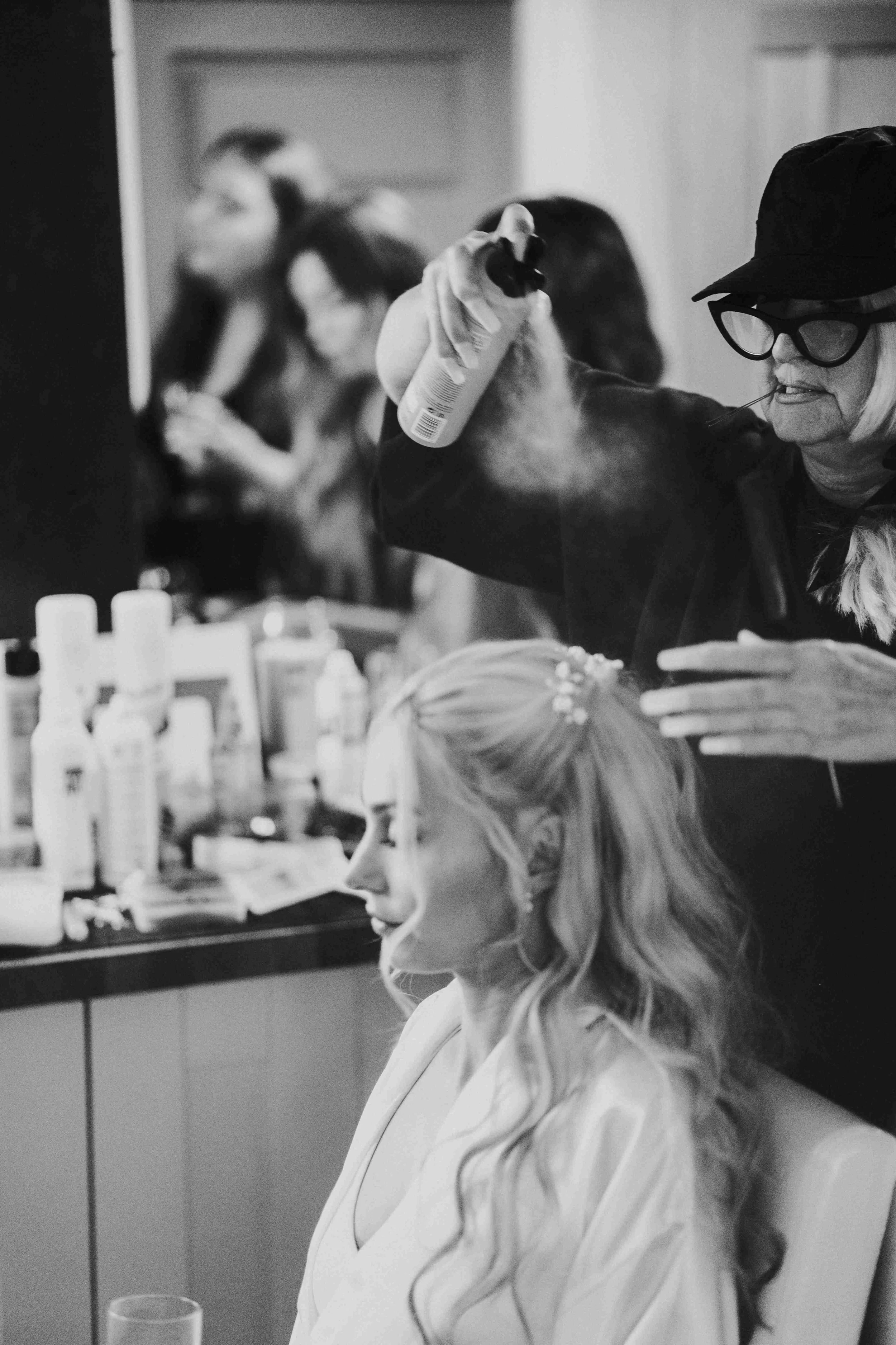 Bride sitting with her eyes closed while hairdresser apply hairspray before her Halfmoon Farm Wedding in Rutland